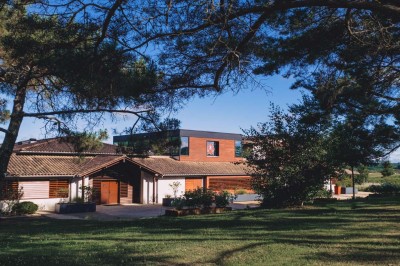 Bâtiment moderne avec façades vitrées et terrasses en bois, entouré de végétation au crépuscule.