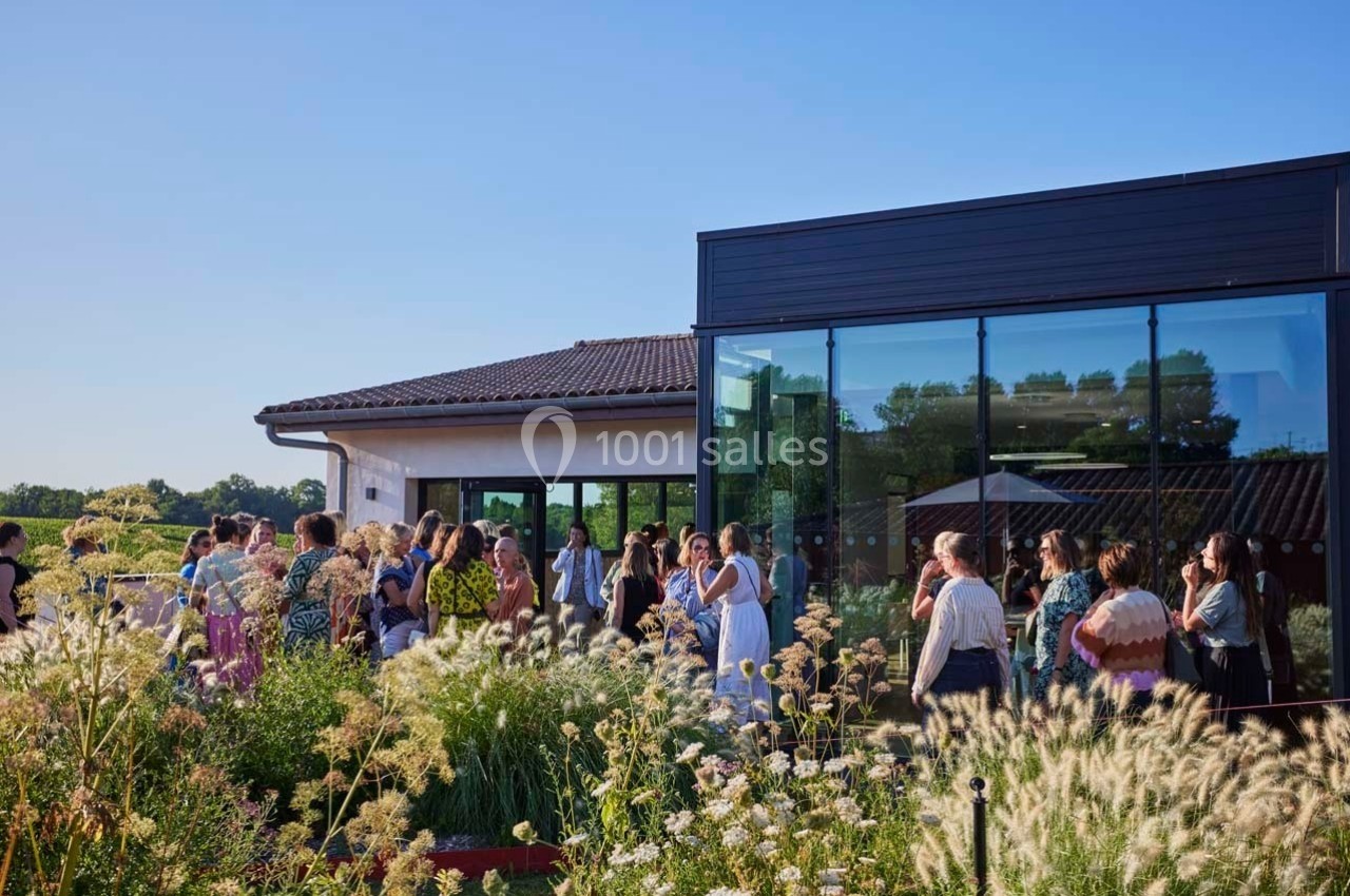 Un groupe de personnes discute à l'extérieur d'un bâtiment moderne entouré de végétation sous un ciel dégagé.