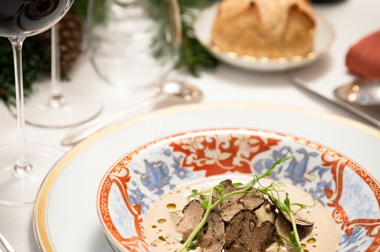 Assiette gastronomique avec truffes en fines lamelles sur une sauce crémeuse, servie sur une table élégamment dressée.