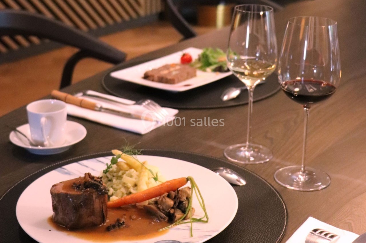 Assiette gastronomique avec viande, légumes et sauce, accompagnée de verres de vin, sur une table élégamment dressée.