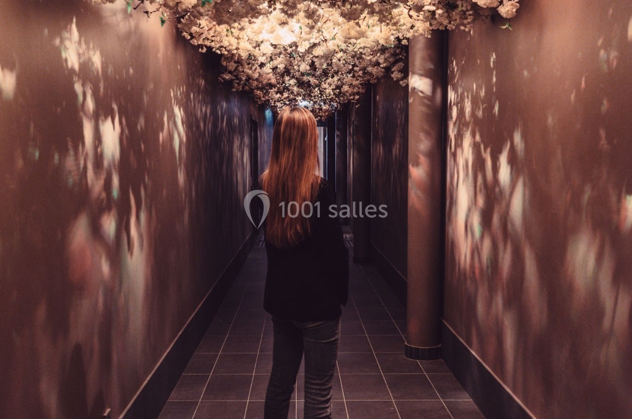 Une femme marche dans un couloir sombre décoré de fleurs blanches suspendues au plafond.