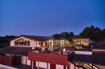 Bâtiment moderne avec façades vitrées et terrasses en bois, entouré de végétation au crépuscule.
