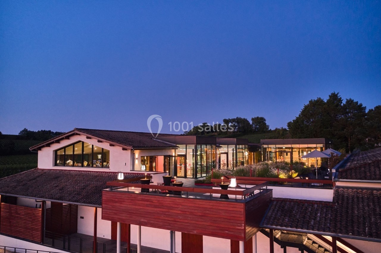 Bâtiment moderne avec façades vitrées et terrasses en bois, entouré de végétation au crépuscule.