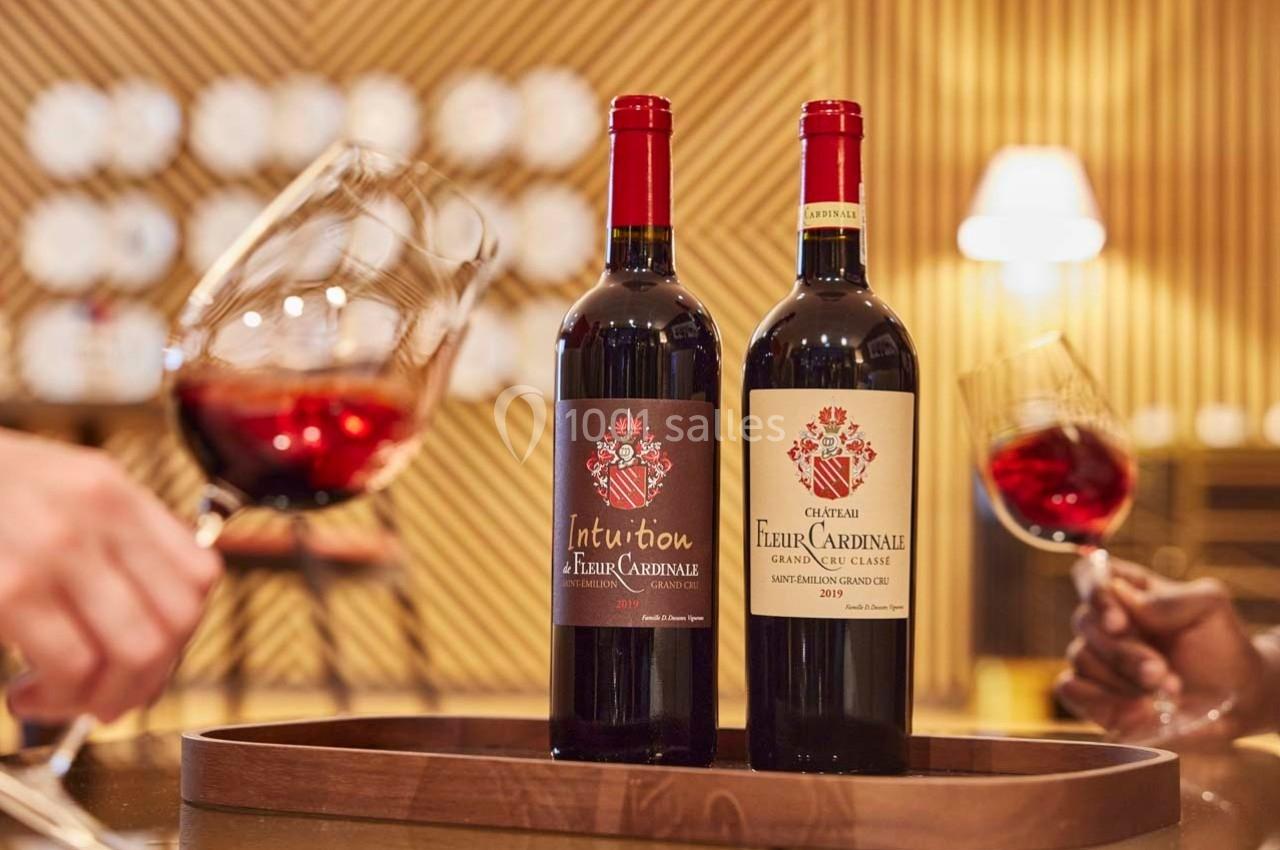 Deux bouteilles de vin rouge posées sur un plateau en bois, entourées de verres de vin dans un décor chaleureux.