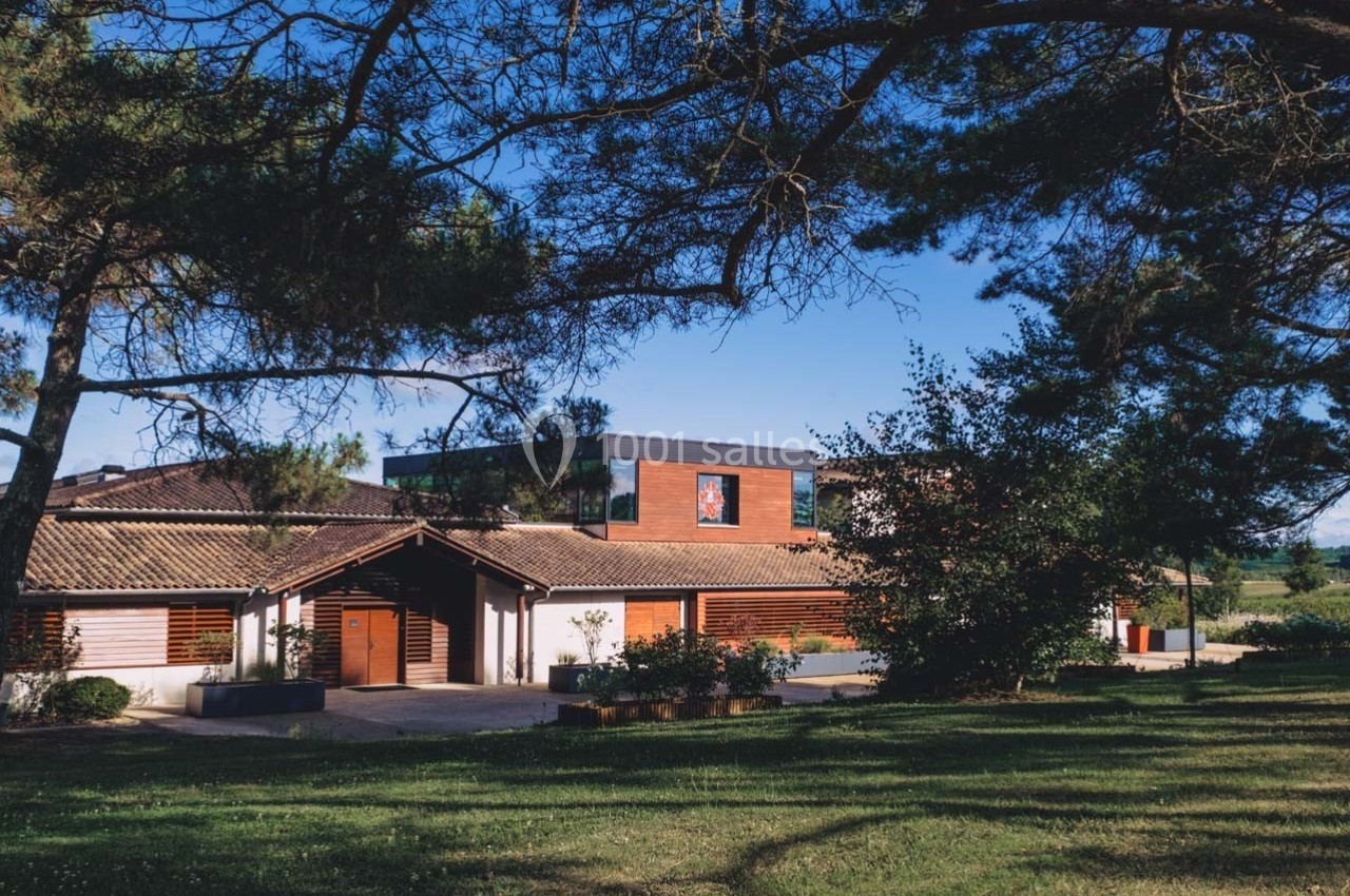 Bâtiment moderne entouré d'arbres, avec un toit en tuiles et une façade en bois, sous un ciel dégagé.