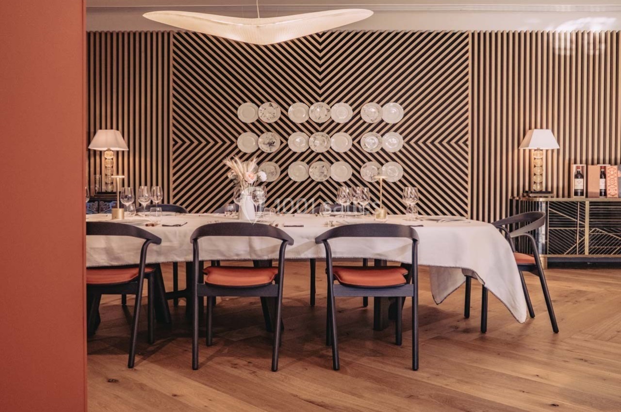 Salle à manger élégante avec table dressée, chaises modernes, parquet en bois et mur décoratif à motifs géométriques.