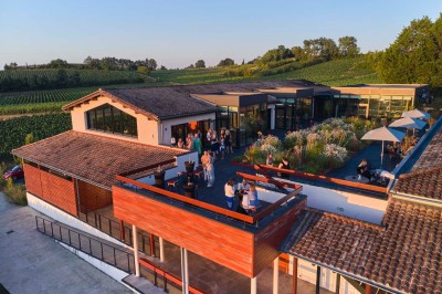 Vue aérienne d'une terrasse animée entourée de vignes au coucher du soleil, avec des invités profitant du cadre.