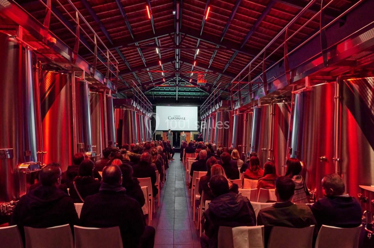 Salle moderne avec des cuves en acier inoxydable, accueillant un public assis face à un écran de projection.