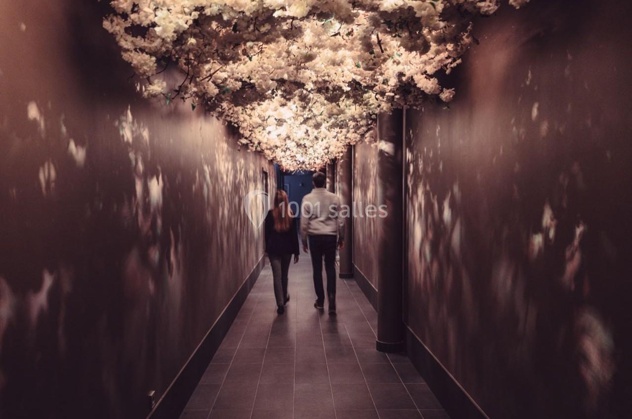Un couple marche dans un couloir sombre décoré de fleurs blanches suspendues au plafond.