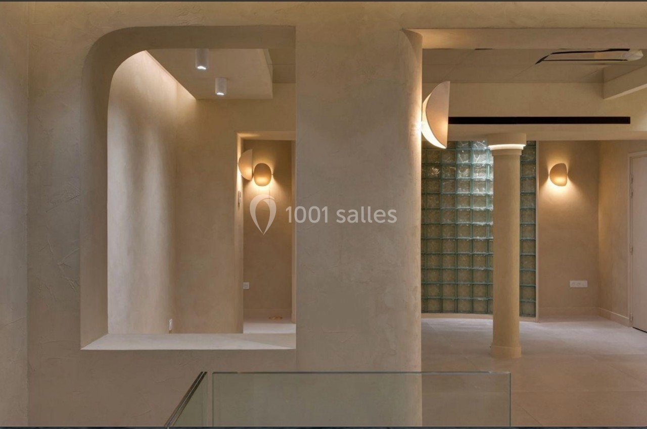 Intérieur minimaliste avec murs beige texturés, éclairage mural doux et cloison en briques de verre.