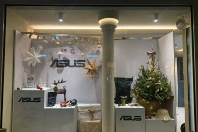 Façade d'une boutique avec vitrines éclairées, affichant des produits ASUS et une pancarte d'accueil pour un événement.