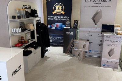 Façade d'une boutique avec vitrines éclairées, affichant des produits ASUS et une pancarte d'accueil pour un événement.