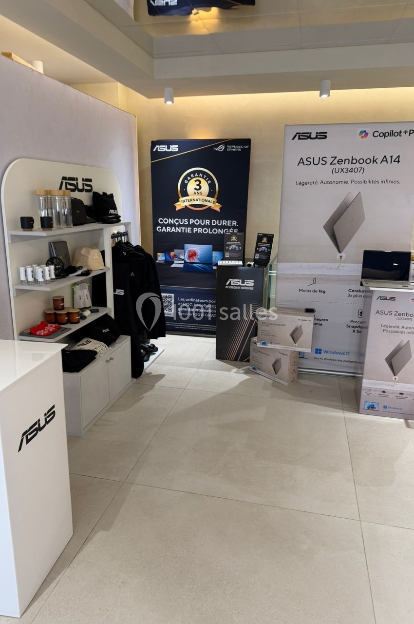Stand promotionnel ASUS présentant des ordinateurs portables, accessoires et affiches publicitaires dans un espace lumineux.