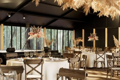 Salle de réception élégante avec tables dressées, décorations florales et grandes baies vitrées donnant sur un paysage boisé.