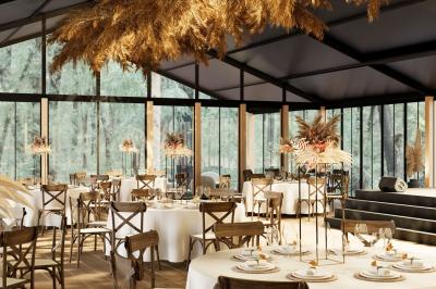 Salle de réception élégante avec tables dressées, décorations florales et grandes baies vitrées donnant sur un paysage boisé.