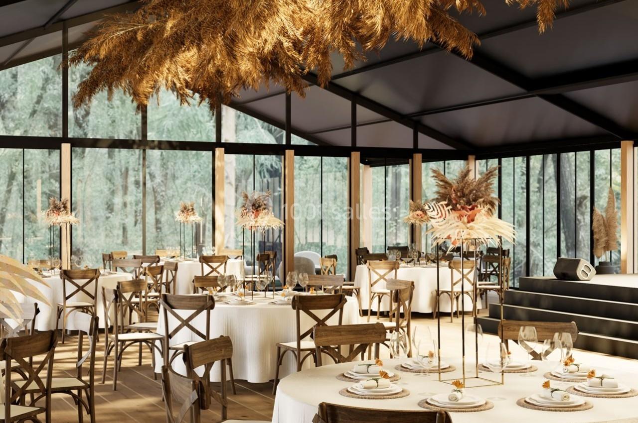 Salle de réception élégante avec tables rondes dressées, décorations florales et grandes baies vitrées donnant sur la nature.