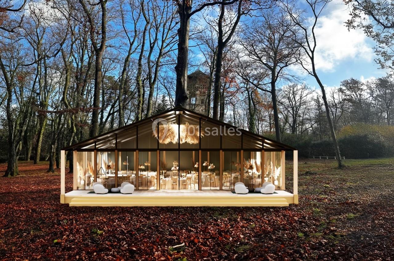 Structure vitrée moderne entourée d'arbres en automne, avec un intérieur aménagé pour un événement.