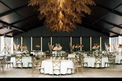Salle de réception élégante avec tables dressées, décorations florales et grandes baies vitrées donnant sur un paysage boisé.