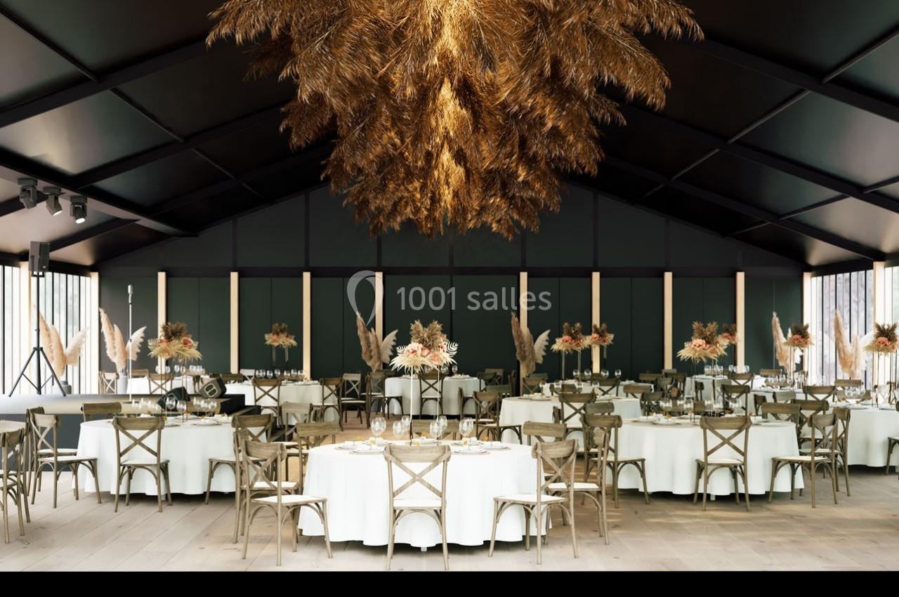 Salle de réception élégante avec tables rondes dressées et décoration suspendue en pampas sous un plafond sombre.