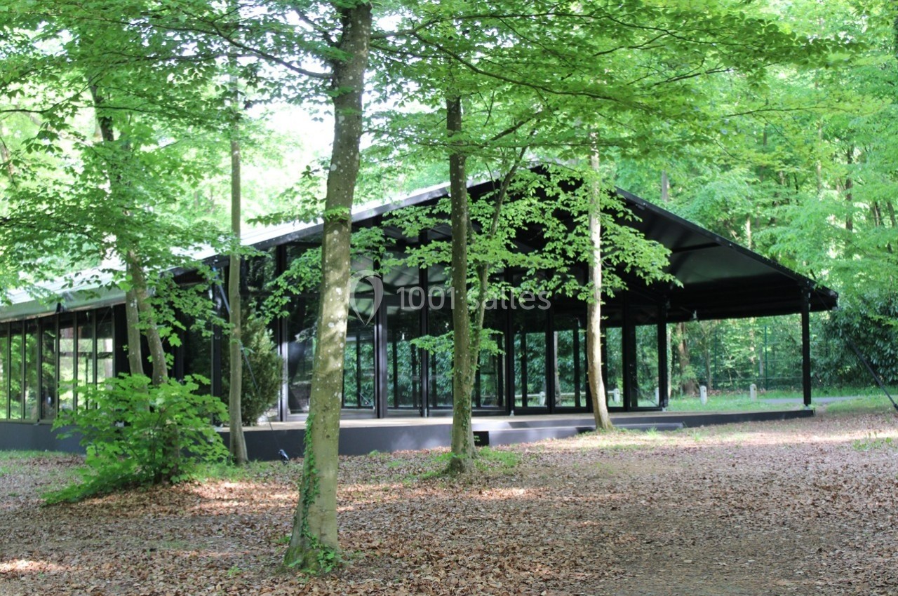 Pavillon moderne en verre et métal entouré d'arbres dans une forêt verdoyante.