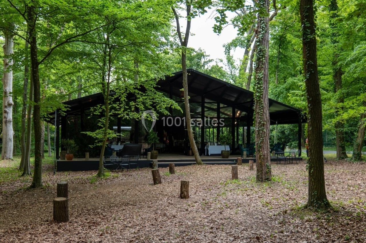 Pavillon moderne en verre et métal entouré d'arbres dans une clairière boisée.