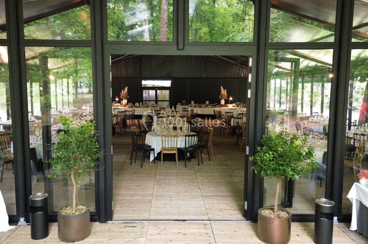 Salle de réception vitrée avec tables décorées, entourée de verdure visible à travers les baies.