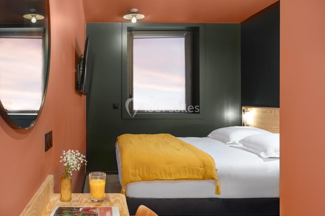 Chambre moderne avec lit double, murs orange, fenêtre avec vue sur le ciel, bureau en bois et décoration minimaliste.