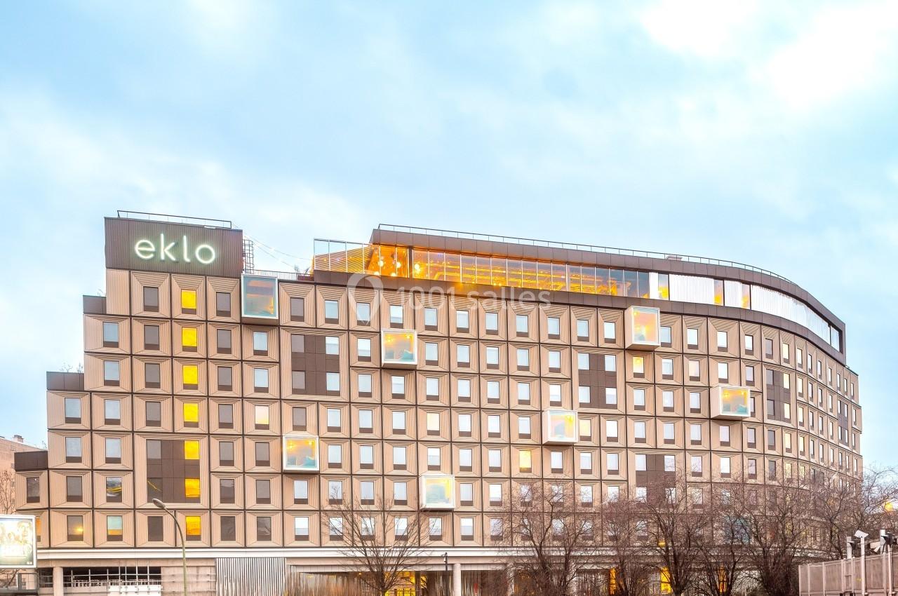 Façade d'un bâtiment moderne avec de nombreuses fenêtres, éclairages intérieurs visibles et enseigne ’eklo’ en haut.