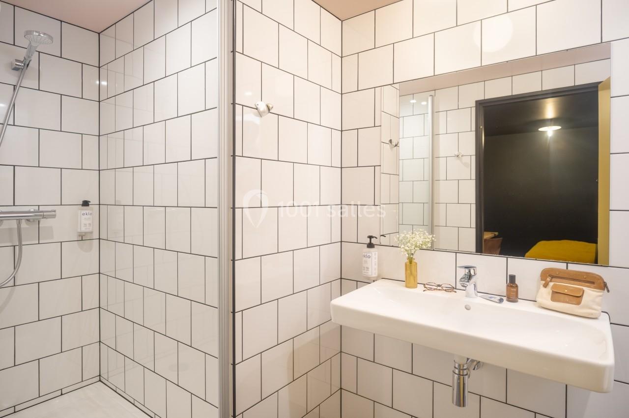 Salle de bain moderne avec douche à l'italienne, carrelage blanc, lavabo suspendu et miroir éclairé.