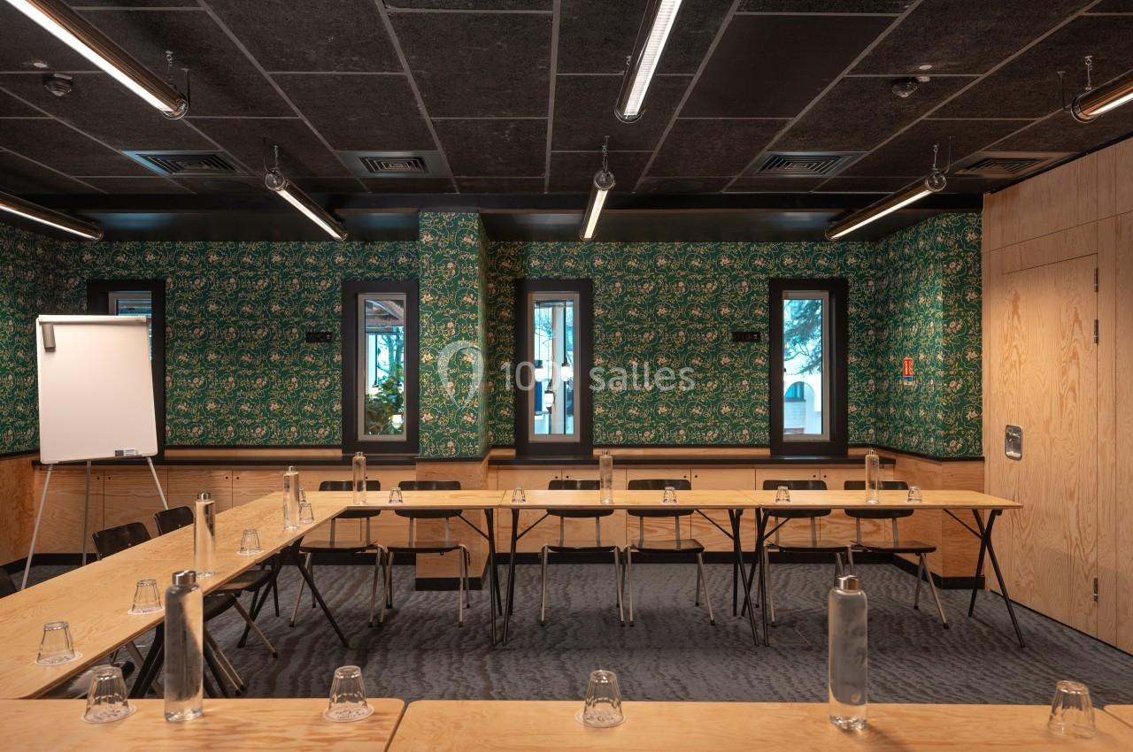 Salle de réunion avec tables en bois disposées en U, bouteilles d'eau et verres, murs décorés de motifs verts.