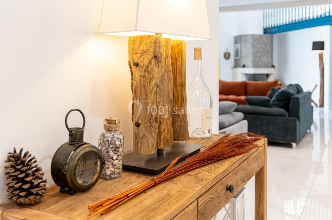 Lampe en bois sur une console en bois avec des objets décoratifs, vue partielle d'un salon en arrière-plan.