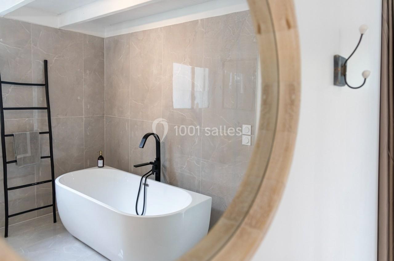 Salle de bain moderne avec baignoire blanche, robinet noir, échelle porte-serviettes et mur en carrelage beige.