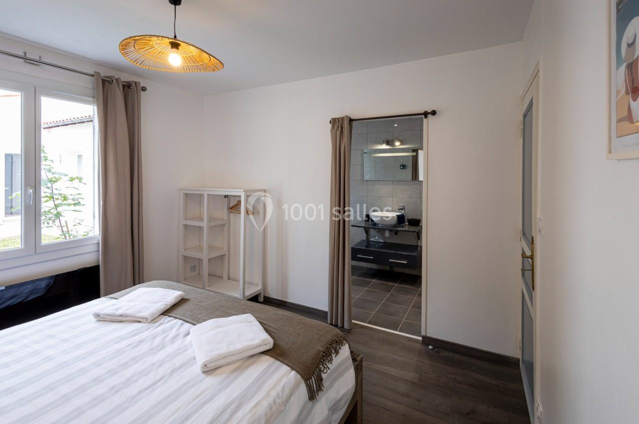 Chambre lumineuse avec lit double, étagère, fenêtre donnant sur l'extérieur et salle de bain attenante avec lavabo moderne.