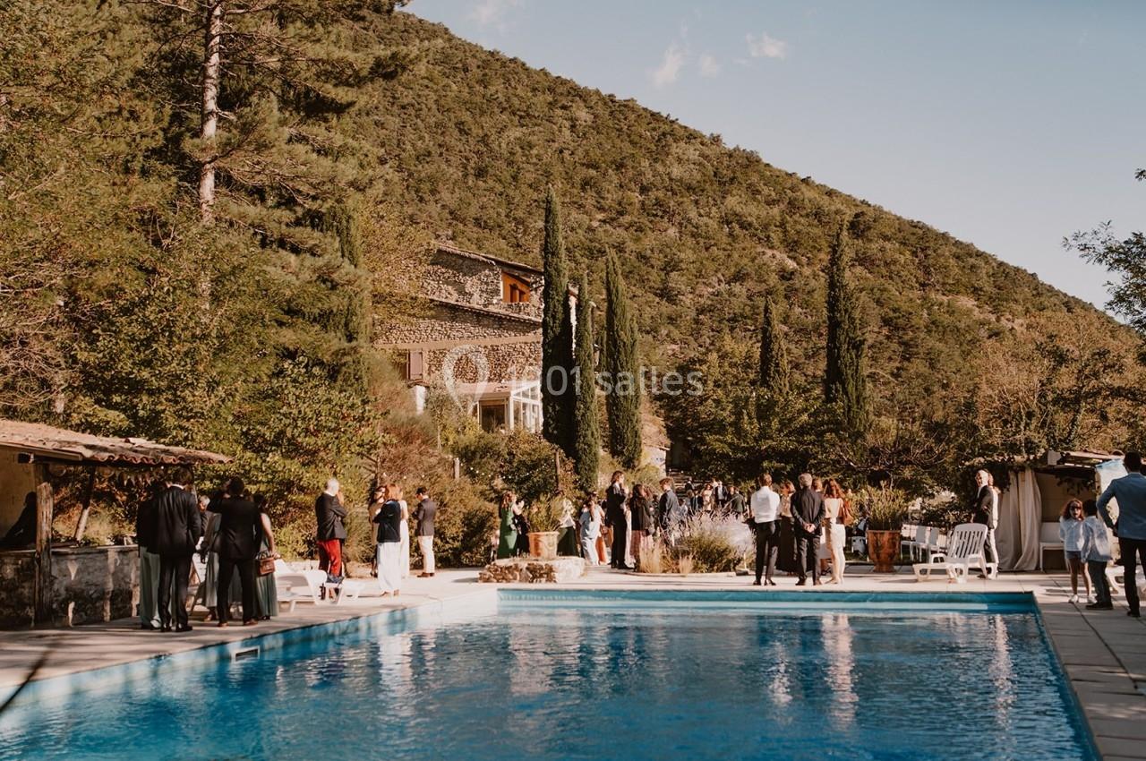 Groupe de personnes rassemblées près d'une piscine dans un cadre naturel avec des collines et des arbres en arrière-plan.