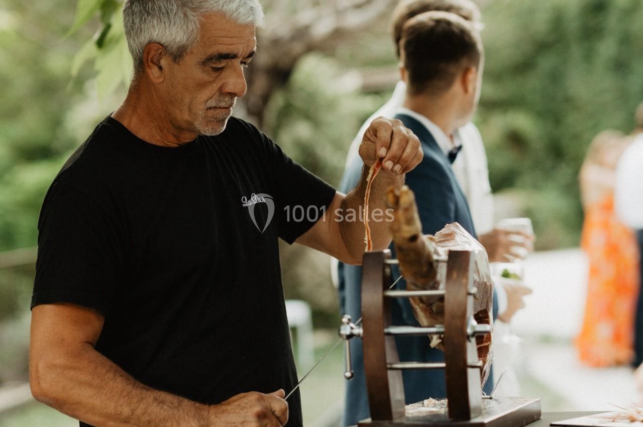 Un homme tranche du jambon sur un support en bois lors d'un événement en plein air.
