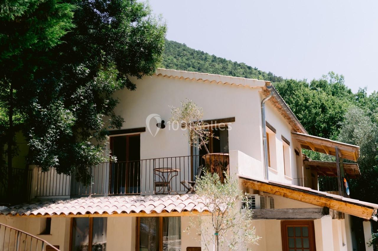 Maison méditerranéenne à deux étages avec balcon, entourée de végétation et éclairée par une lumière naturelle.