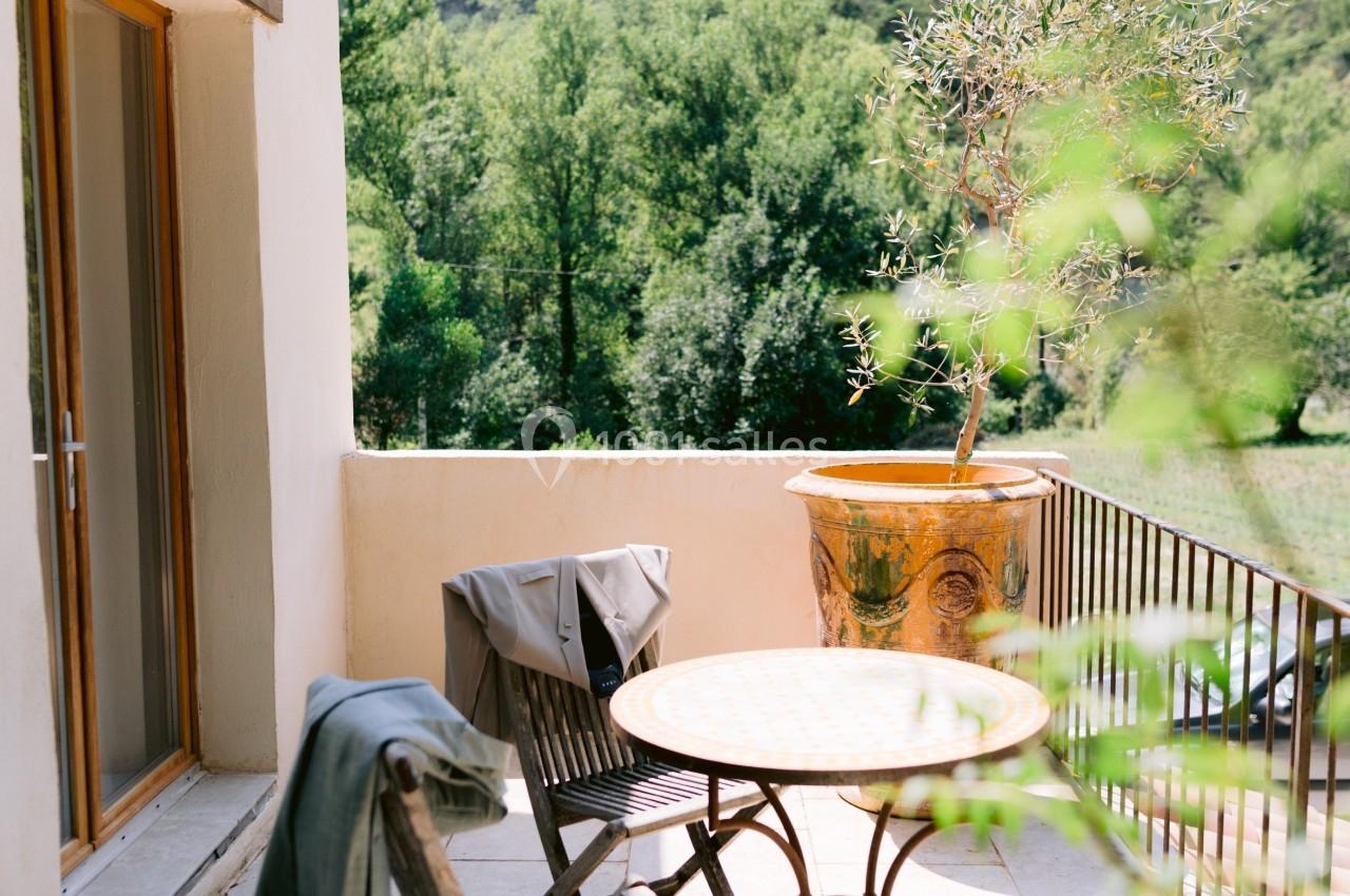 Terrasse ensoleillée avec table ronde, chaises en bois, pot en terre cuite et vue sur des collines verdoyantes.