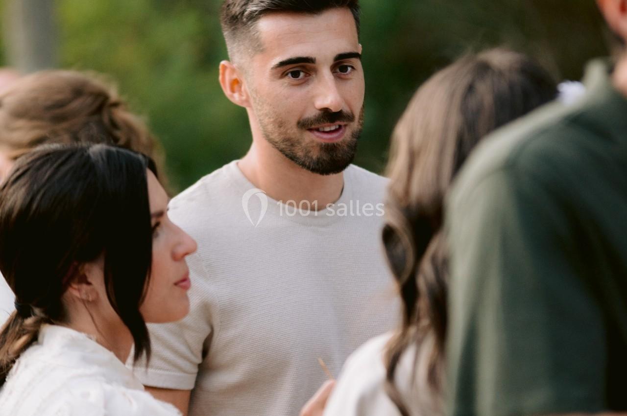 Un homme debout parmi un groupe de personnes discutant en extérieur, avec un fond de verdure flou.