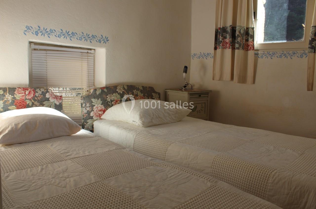 Deux lits simples avec couvre-lits blancs dans une chambre lumineuse, décorée de motifs floraux et équipée d'une petite…