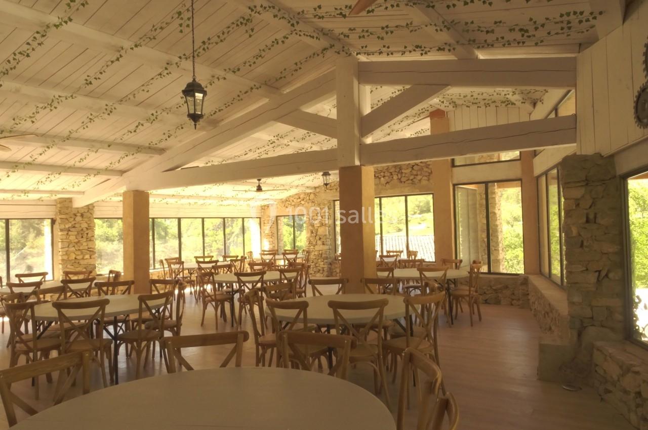 Salle lumineuse avec tables et chaises en bois, grandes baies vitrées et plafond décoré de motifs végétaux.