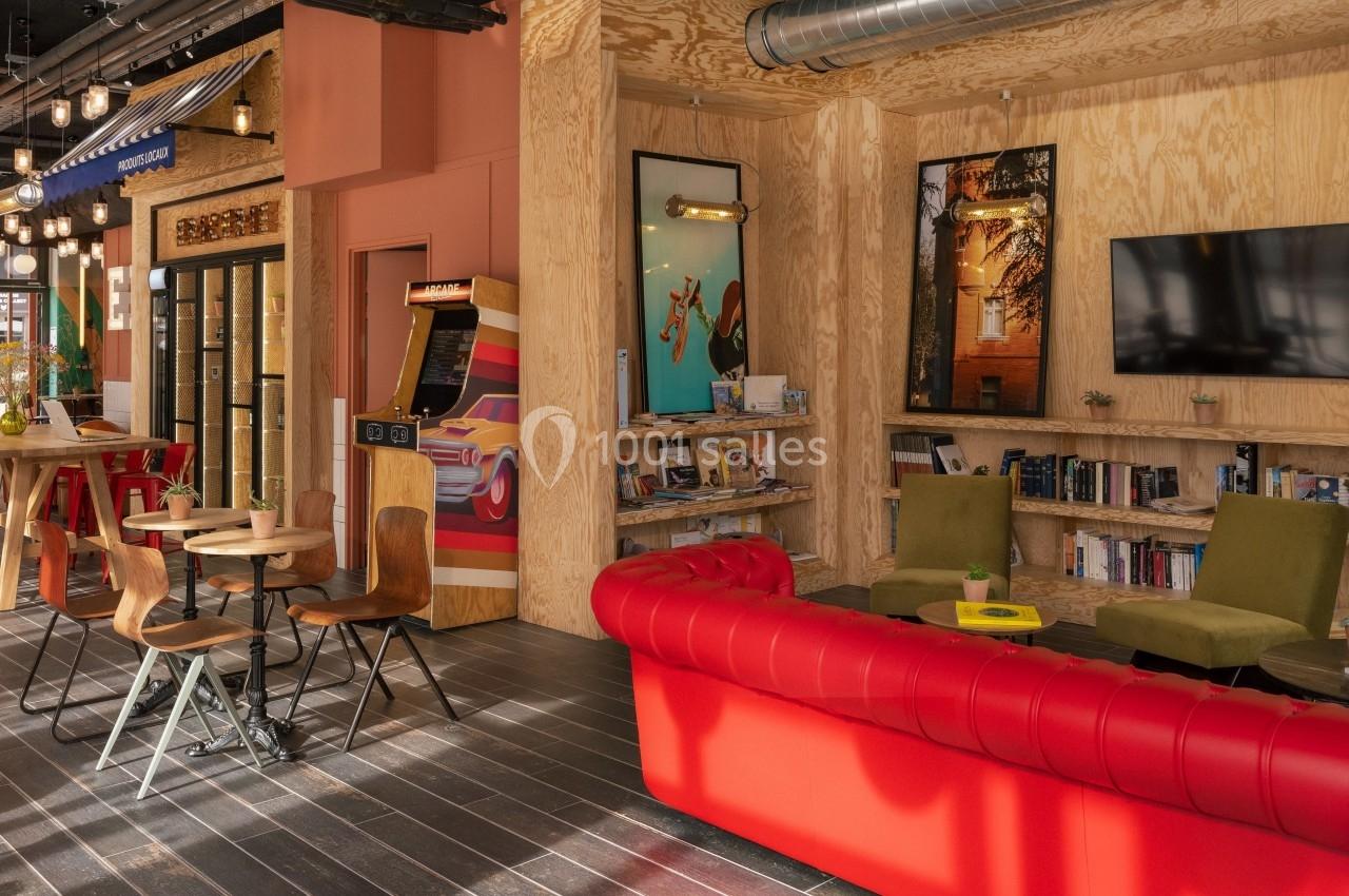 Espace intérieur chaleureux avec canapé rouge, étagères remplies de livres, tables en bois et décorations modernes.