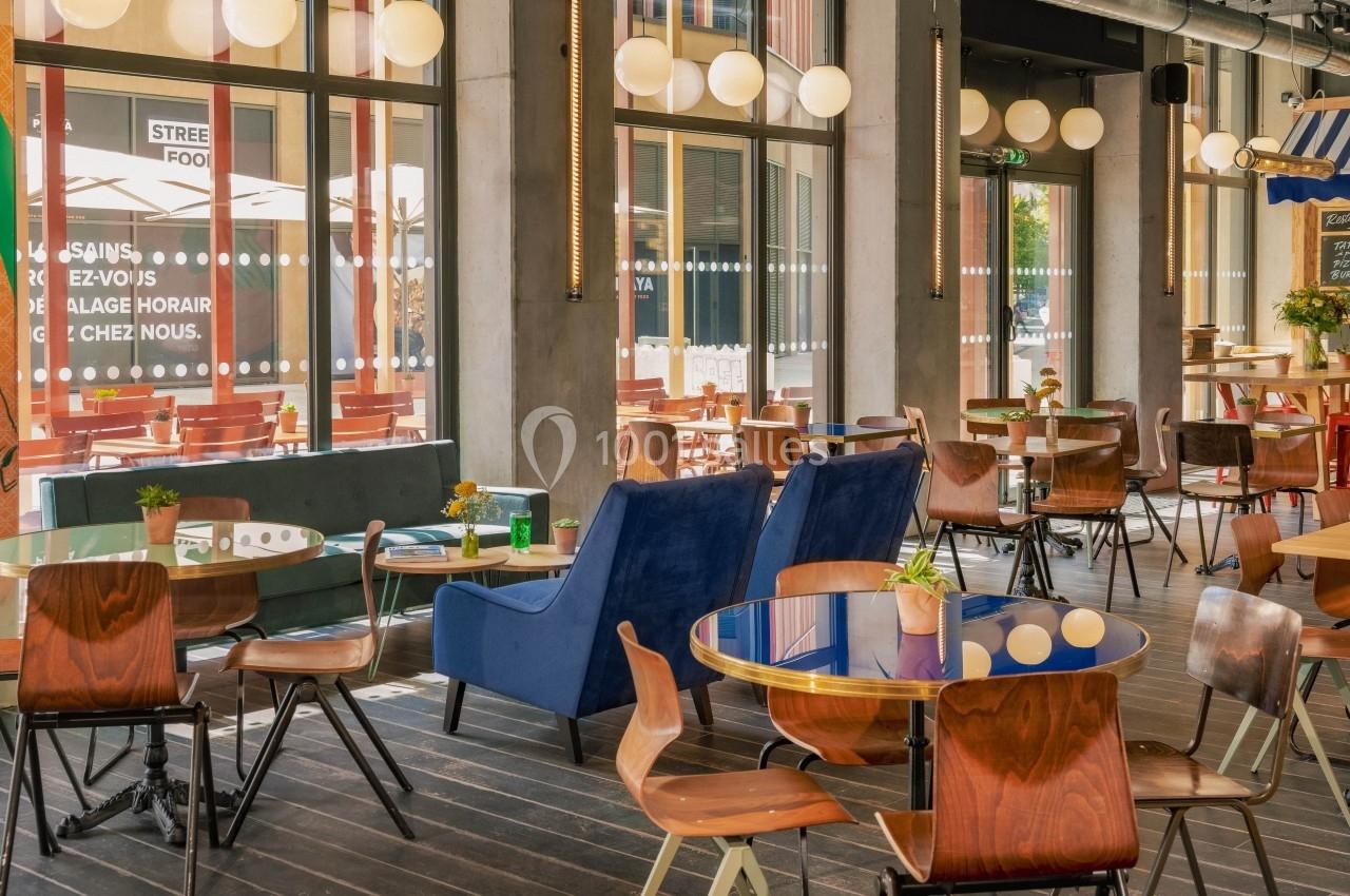 Salle de restaurant lumineuse avec des tables en bois, des chaises variées et une décoration moderne.