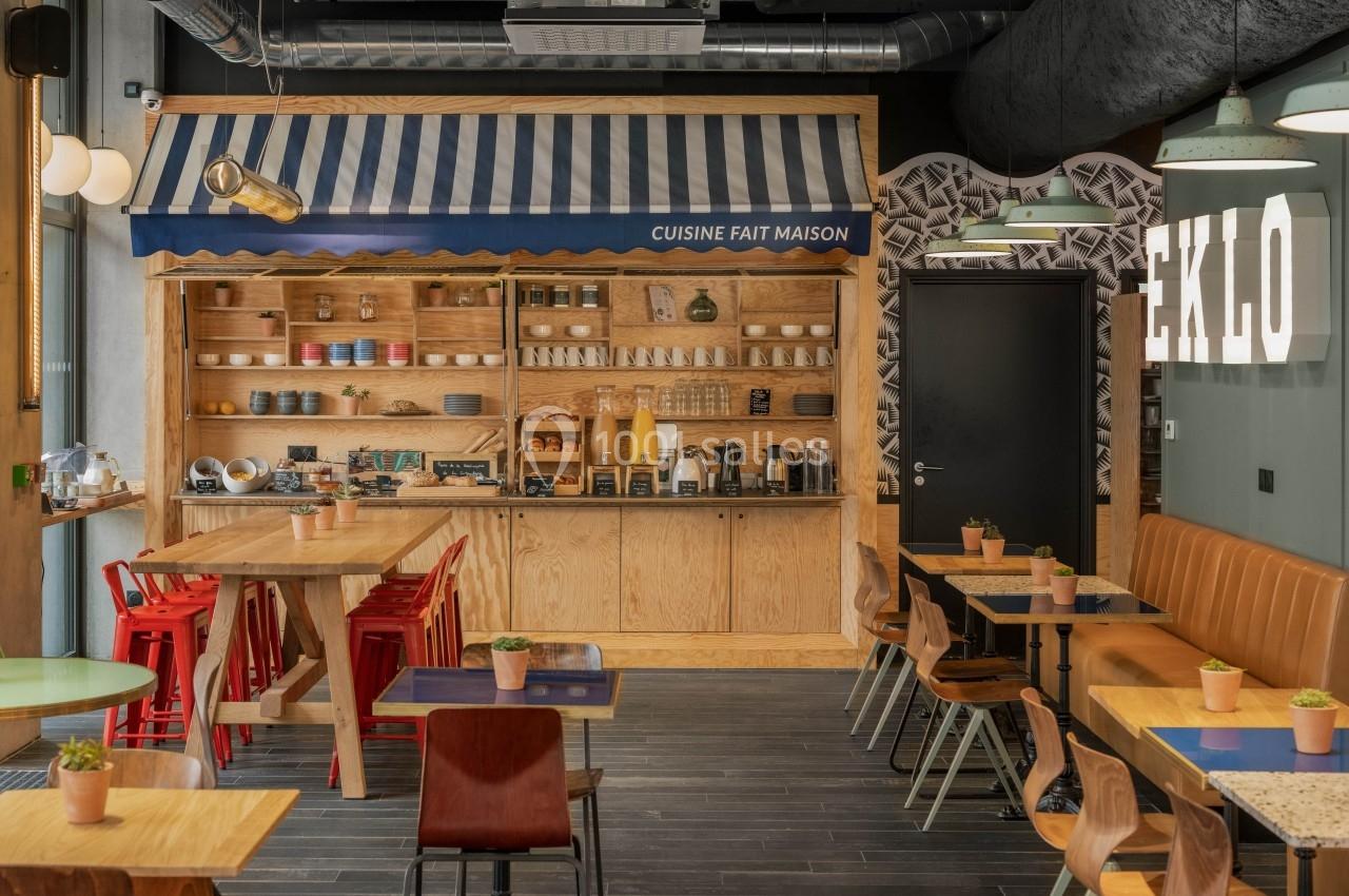 Salle de restaurant lumineuse avec tables en bois, chaises colorées et un comptoir décoré d'une enseigne ’Cuisine fait…
