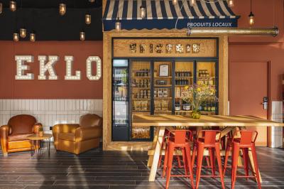 Façade d'un bâtiment moderne avec une enseigne lumineuse ’eklo’, des baies vitrées et des tables en terrasse.