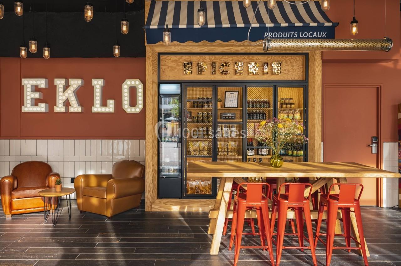 Coin boutique avec étagères de produits locaux, table en bois, chaises rouges et décor lumineux dans un espace chaleureux.