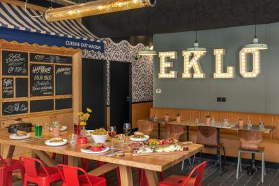 Façade d'un bâtiment moderne avec une enseigne lumineuse ’eklo’, des baies vitrées et des tables en terrasse.