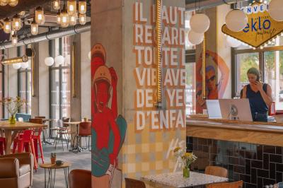 Façade d'un bâtiment moderne avec une enseigne lumineuse ’eklo’, des baies vitrées et des tables en terrasse.