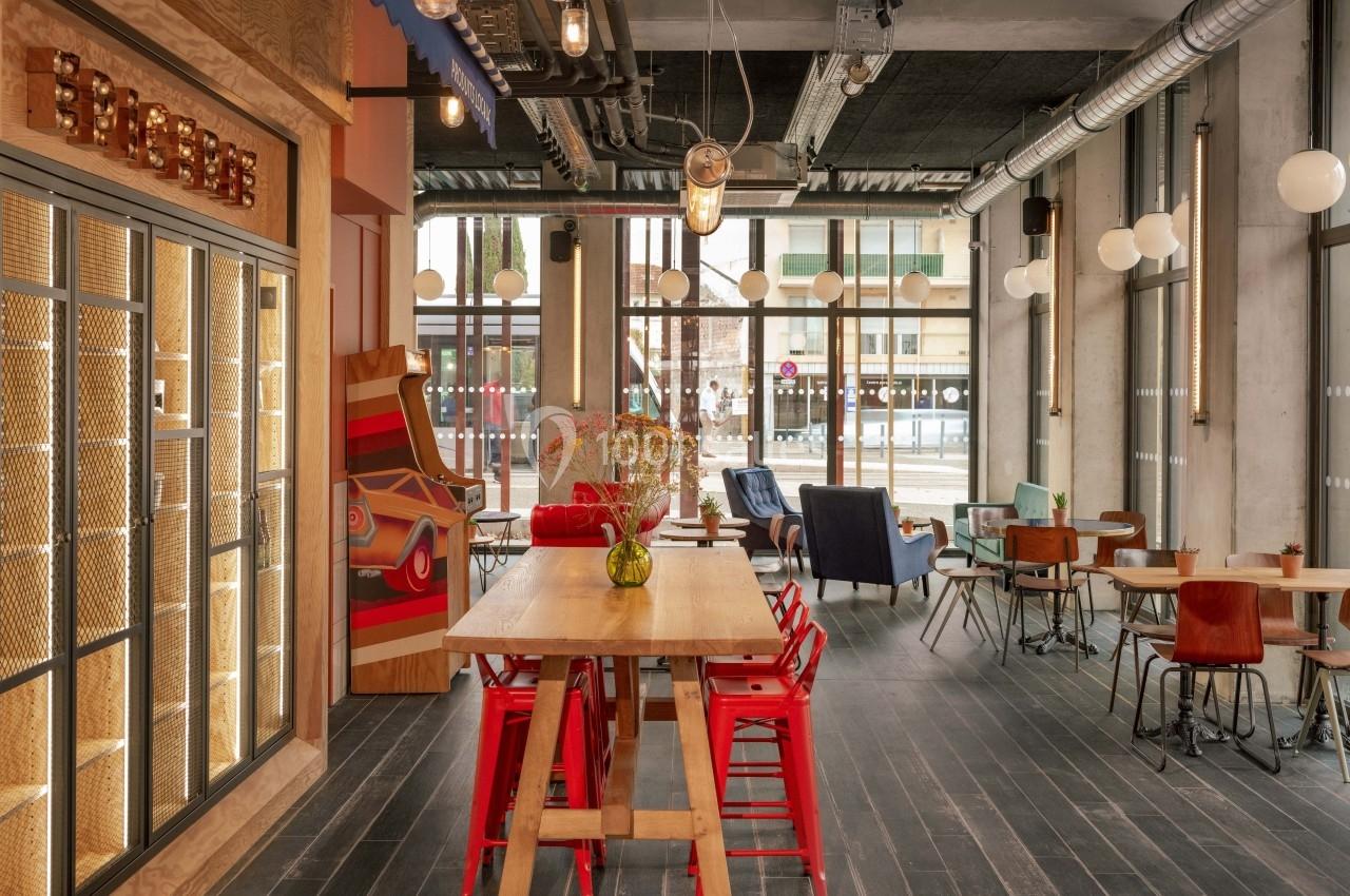 Salle lumineuse avec mobilier éclectique, grandes baies vitrées, chaises colorées et décoration moderne industrielle.