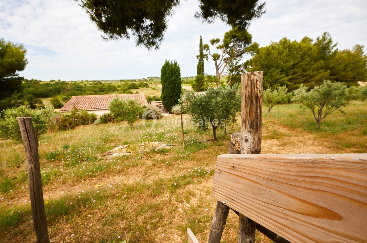 Paysage rural avec une maison en tuiles rouges entourée d'arbres, de champs et d'une clôture en bois au premier plan.