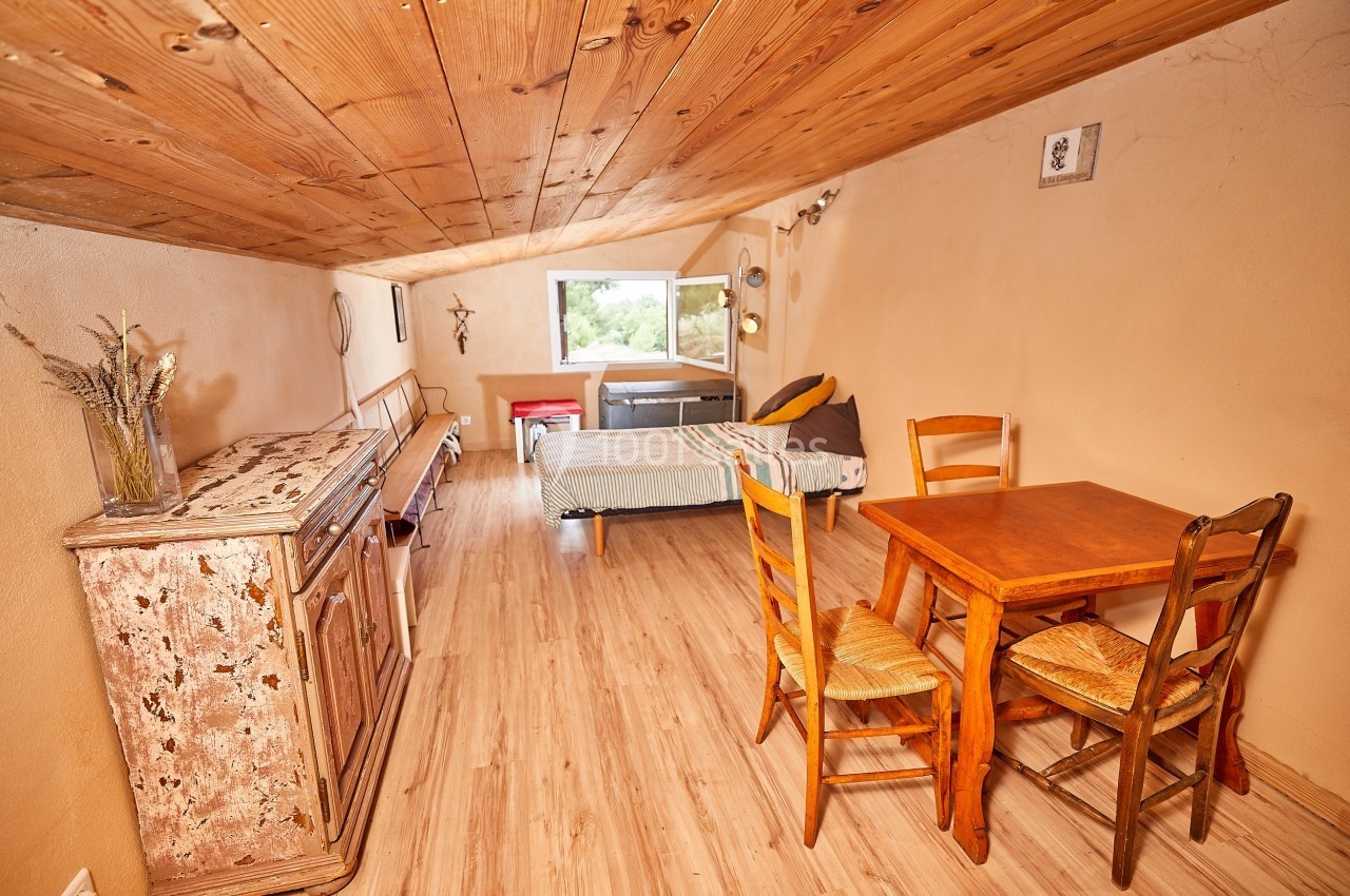 Pièce mansardée avec un lit, une table en bois, des chaises et un buffet ancien, éclairée par une fenêtre.